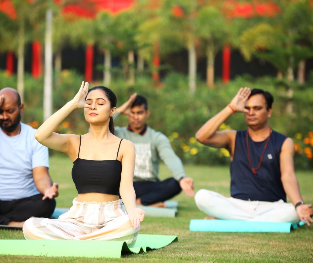 Group of people practicing yoga outdoors in a peaceful natural setting, surrounded by trees and greenery, promoting relaxation and mindfulness.
